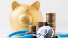   A piggy bank next to a pile of coins and a stethoscope.