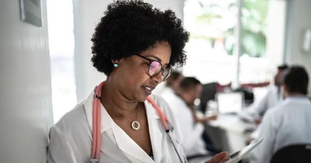 Healthcare provider standing against a wall and looking at something in their hand