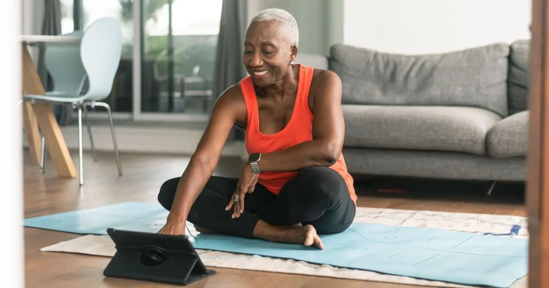 A woman sitting on a yoga mat using a tablet